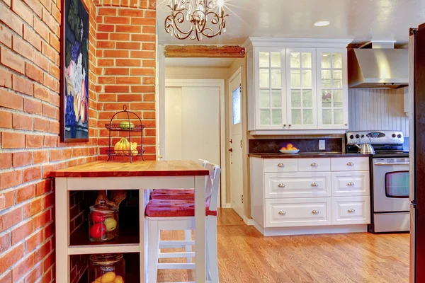 White kitchen with brick wall, hardwood and stainless steal stove.