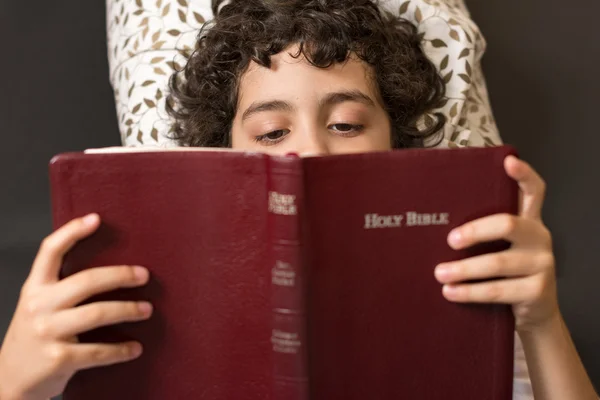 Young child reading the bible in bed. Boy laying of the floor and reading the Holy Bible. The word of god being read by a small kid