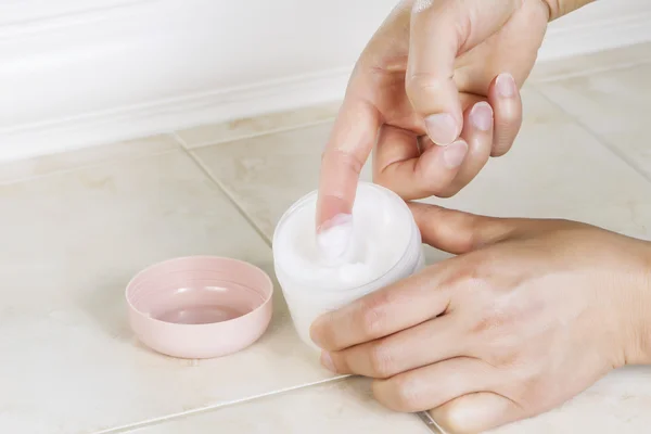 Female index finger dipping into cosmetic cream from open jar