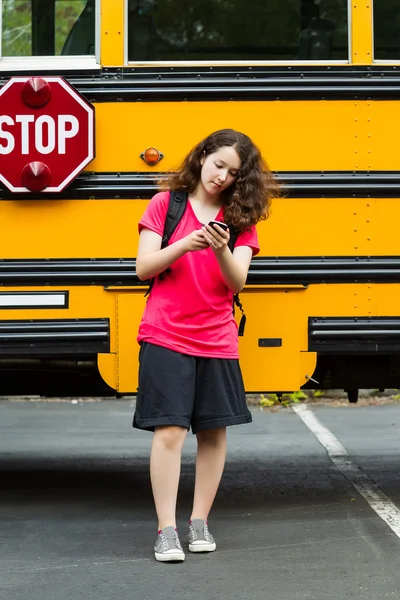 Girl walking away from School Bus while texting on her phone