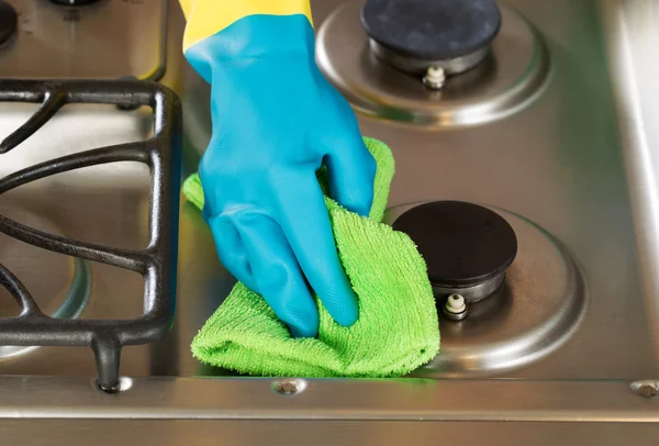 Gloved hand wiping down stove top range with green microfiber ra