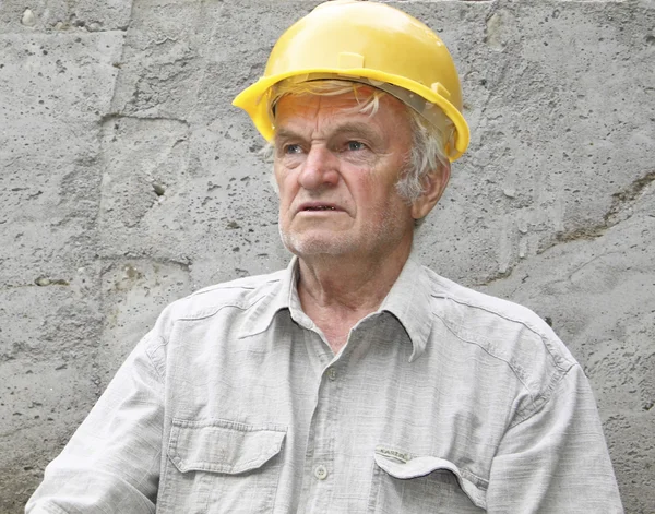 The man in a yellow helmet against a concrete wall looks afar