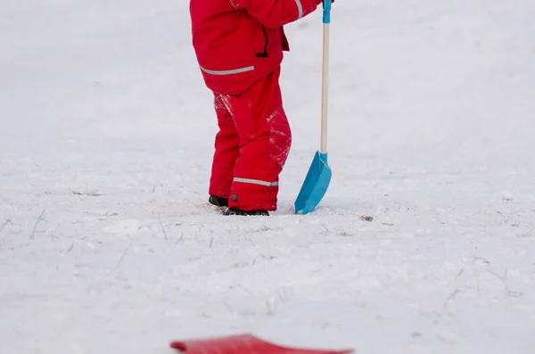 Child stand with snow shovel in waterproof wear