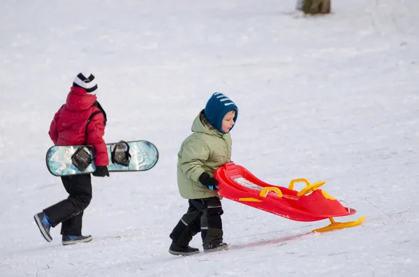 Children with snowboard and sledge with handlebar