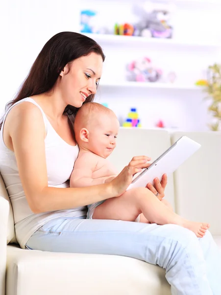 Mother and baby child are looking to play and read tablet computer on the couch at home