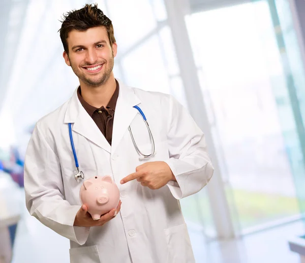 Portrait Of A Young Doctor Holding A Piggy Bank