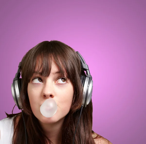 Portrait of young woman listening to music with bubble gum over