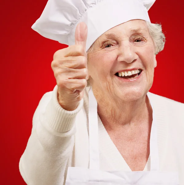 Portrait of cook senior woman doing approval gesture over red ba