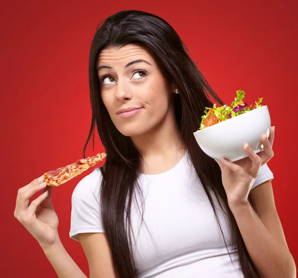 Portrait of young woman choosing pizza or salad against a red ba
