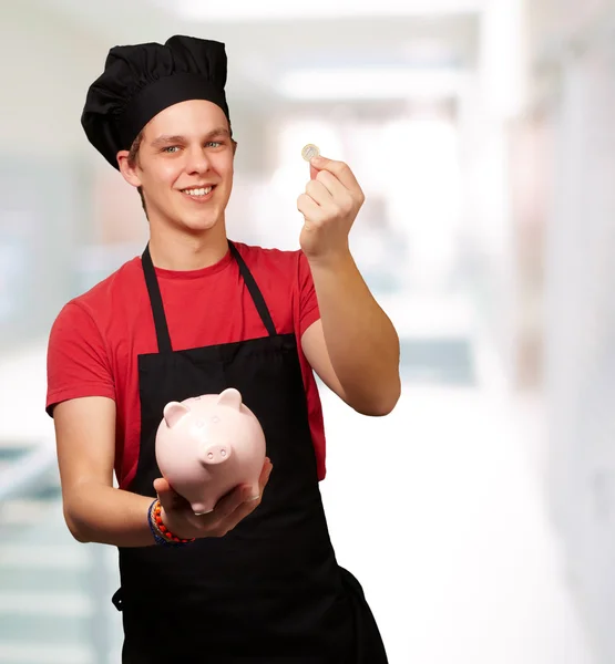 Portrait of young cook man holding euro coin and piggy bank indo