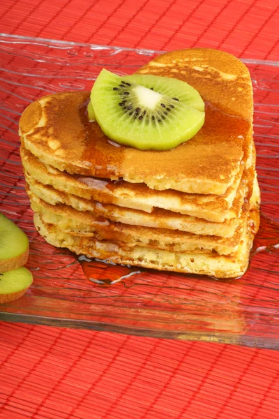 Stack of heart-shaped pancakes with syrup and kiwi fruit