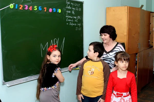 The teacher near a blackboard explains to children a lesson