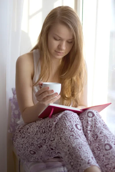 Girl on the window sill with a cup of reading book