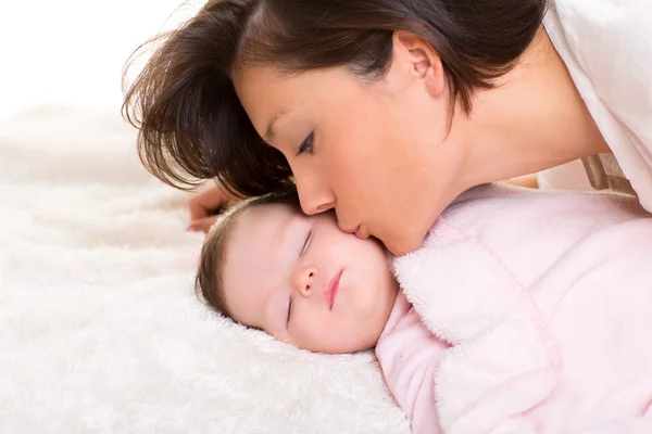 Baby girl and mother kissing her lying happy on white
