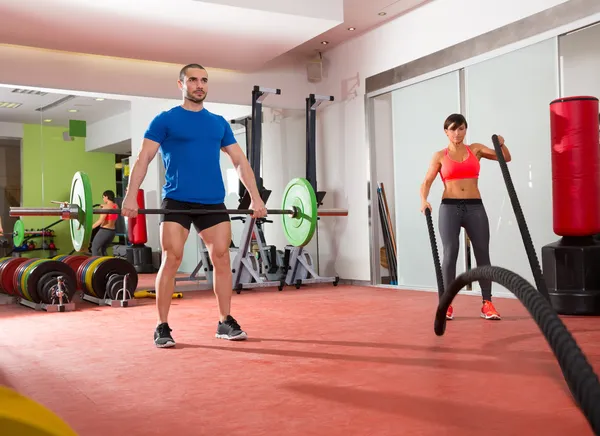 Crossfit gym weight lifting bar man woman battling ropes