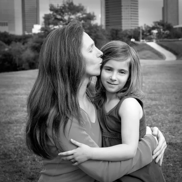 Mother and daughter happy hug kiss in park at city skyline