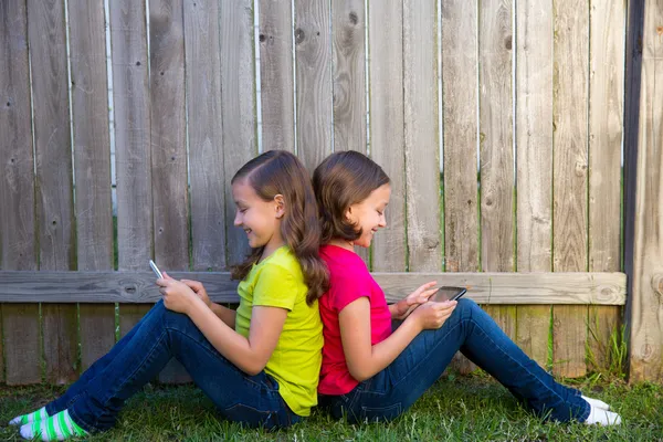 Twin sister girls playing tablet pc sitting on backyard lawn