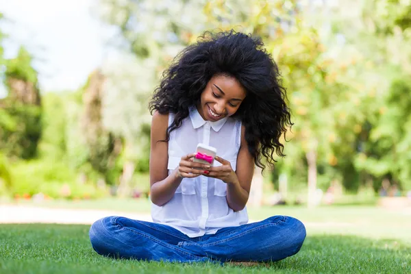 Teenage black girl using a phone, lying on the grass - African p