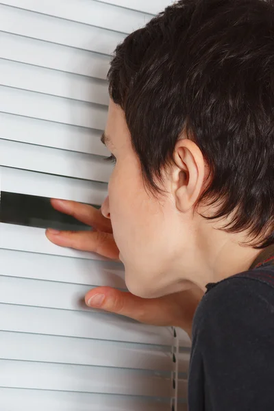 Young woman looking through the blinds of a light room