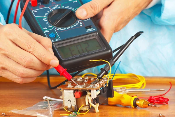 Serviceman checks electronic components of device with multimeter