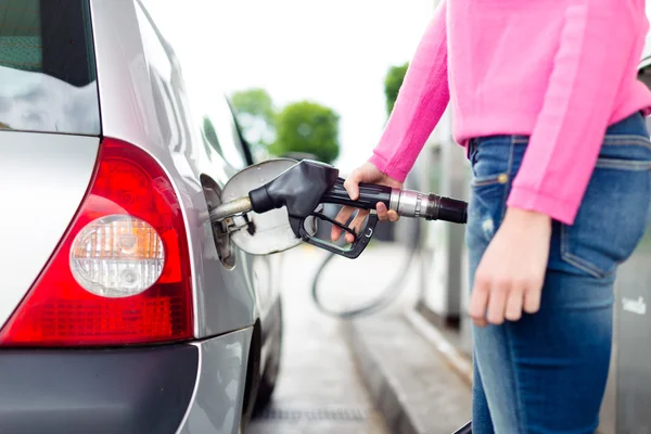 Lady pumping gasoline fuel in car at gas station.