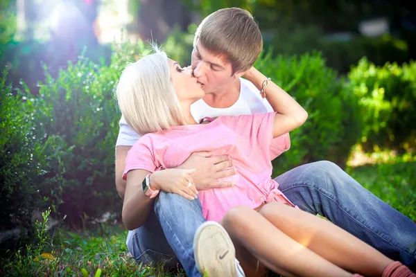 Muscular man hugging and kissing blonde woman on grass