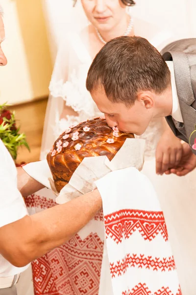 Handsome groom kissing loaf of bread by tradition