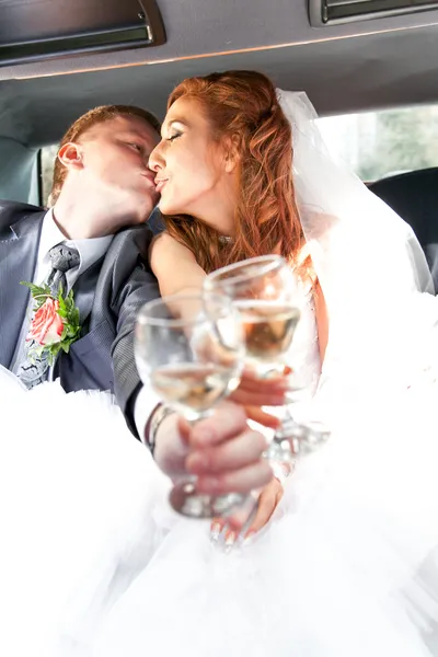 Bride and groom kissing in car and clinking glasses
