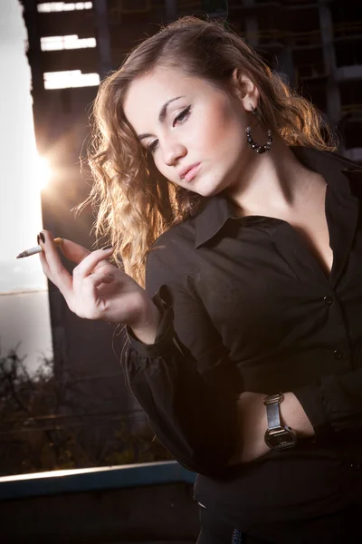 Woman in black shirt holding and smoking cigarette against city