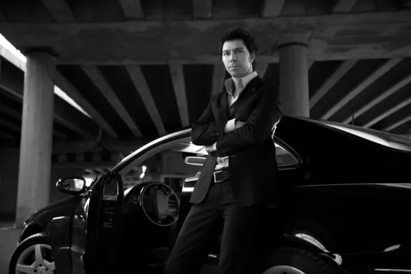 Portrait of handsome man in suit leaning against black super car