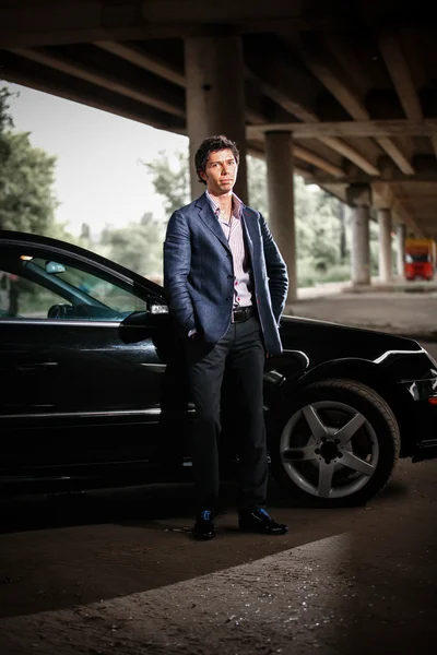 Elegant man in suit posing against black luxury car