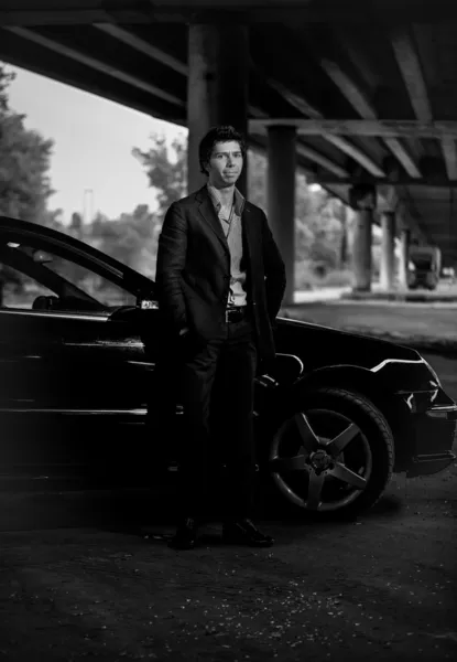 Photo of young handsome man posing against black luxury car