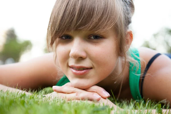 Portrait of young woman lying on grass and holding hands under chin