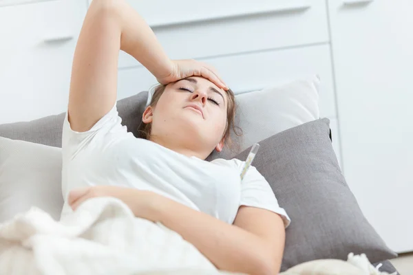 Portrait of sick woman lying in bed and holding hand on head