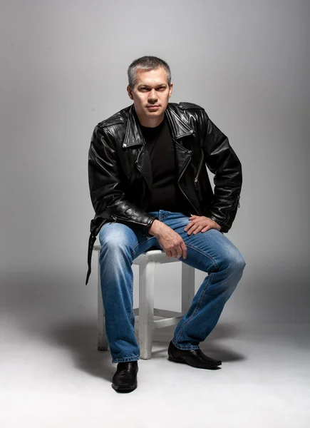 Adult man in leather jacket sitting on white chair