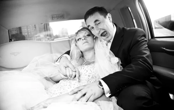 Young funny groom hugging bride on backseat and winking at camera