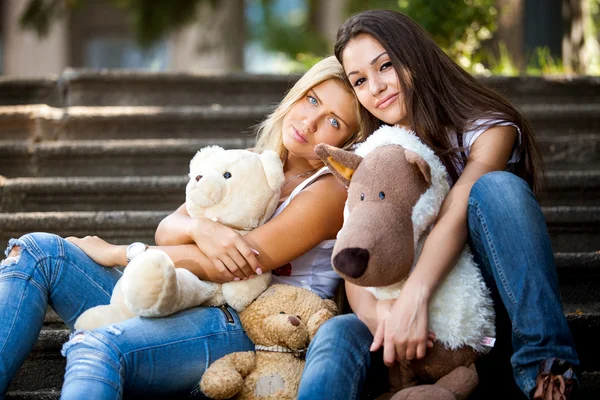Portrait of two beautiful girls sitting on stairs with teddy bears