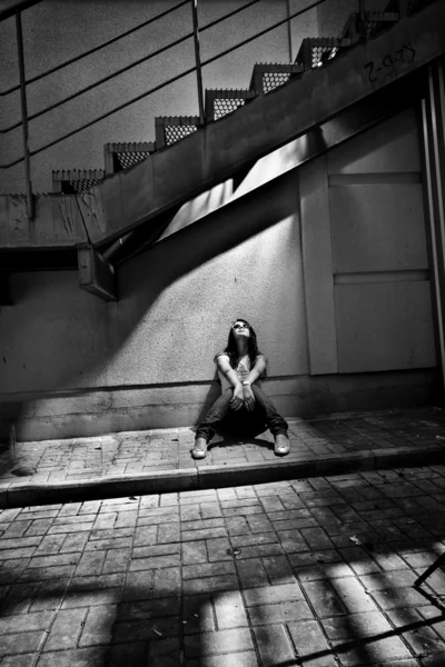 Woman sitting under metal staircase in beam of light