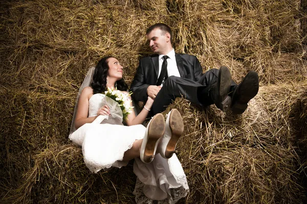 Just married couple holding hands and sitting on hay at stable