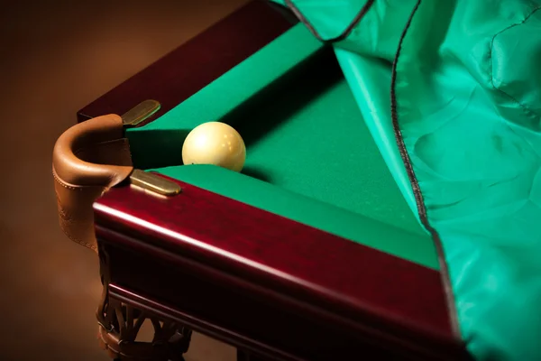 Ball in billiard pocket on partly covered table