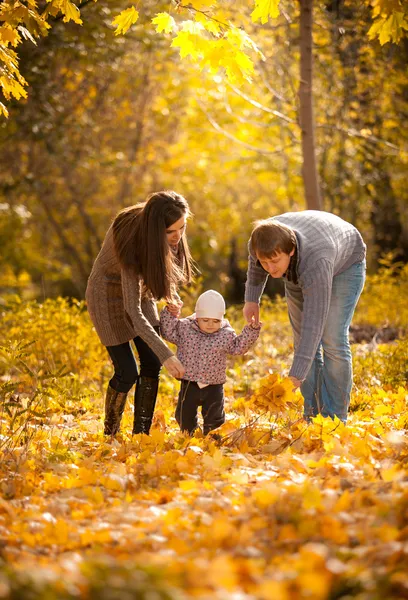 Parents teaching small daughter to walk at autumn park