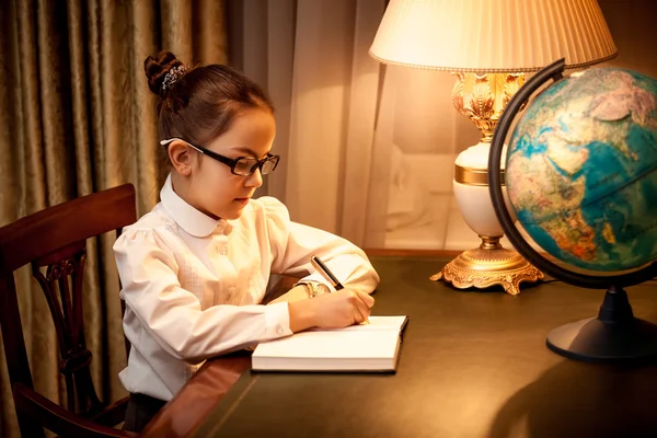 Girl writing in notebook at desk with lamp and globe