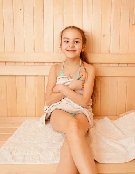 Smiling little girl sitting on bench at sauna