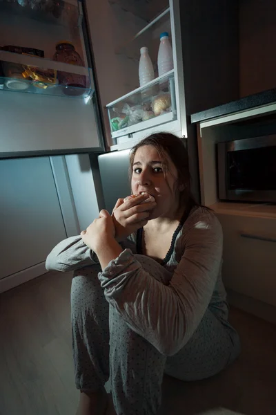 Woman eating on floor at kitchen in night