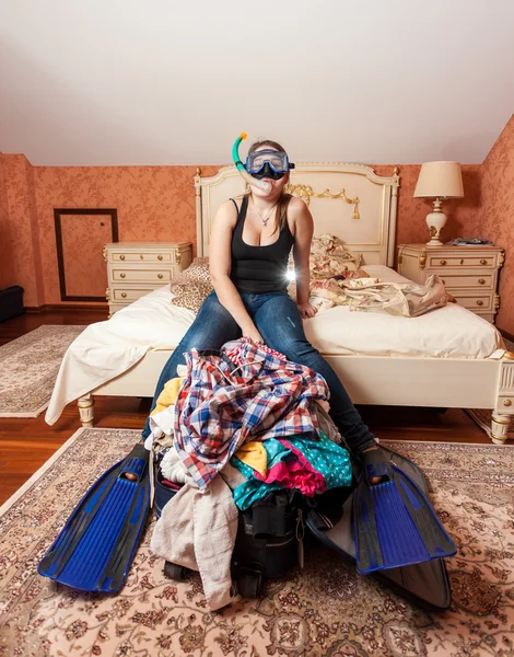 Woman in flippers and mask sitting on packed suitcase