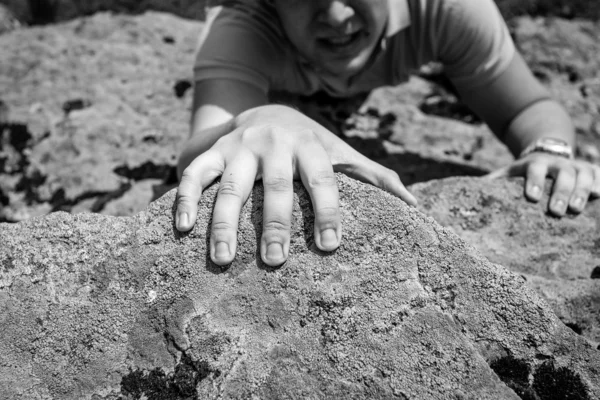 Closeup photo of man holding on cliff on one hand