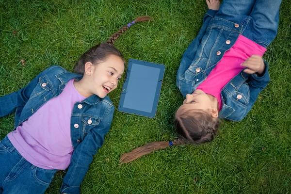 Little girls lying face to face on grass and looking at tablet