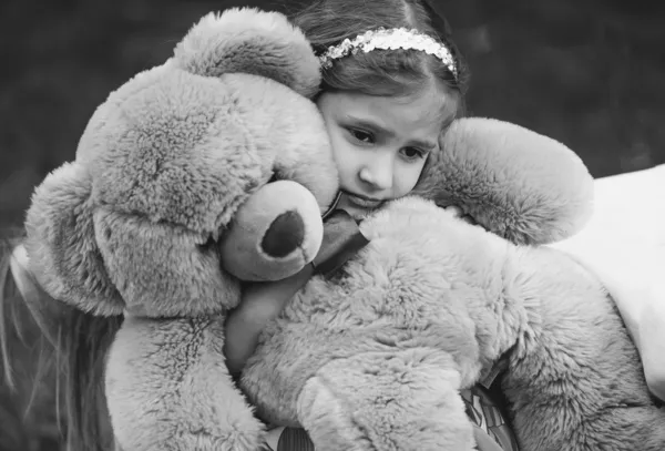 Monochrome portrait of small crying girl hugging teddy bear