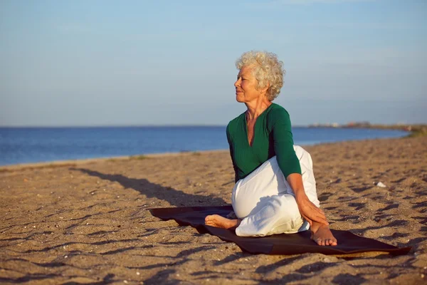 Senior woman performing a yoga routine on the beach
