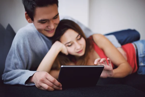Romantic young couple lying on couch using tablet